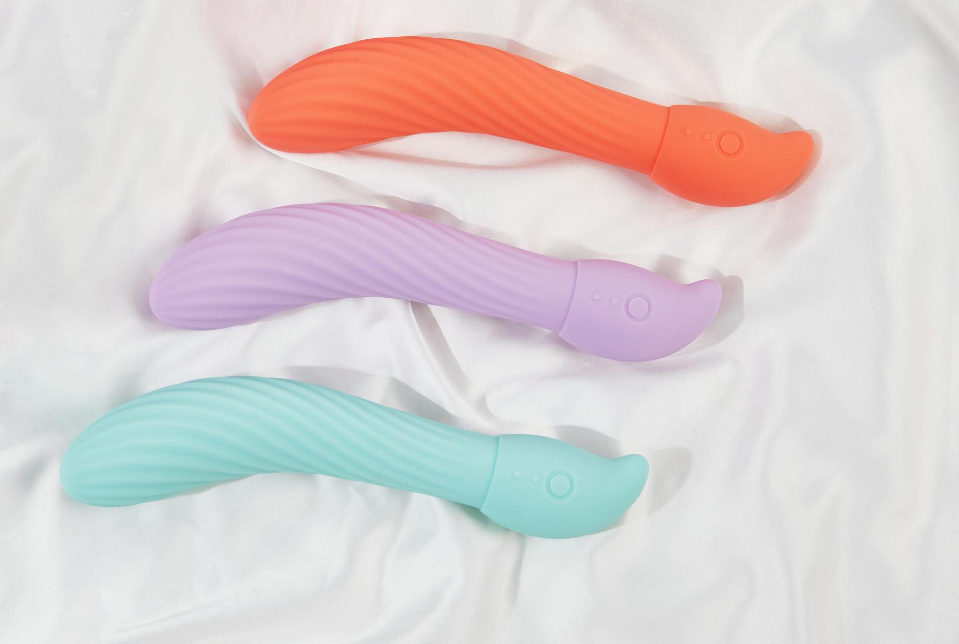 A hand holding a modern orange vibrator against a minimalist purple backdrop.