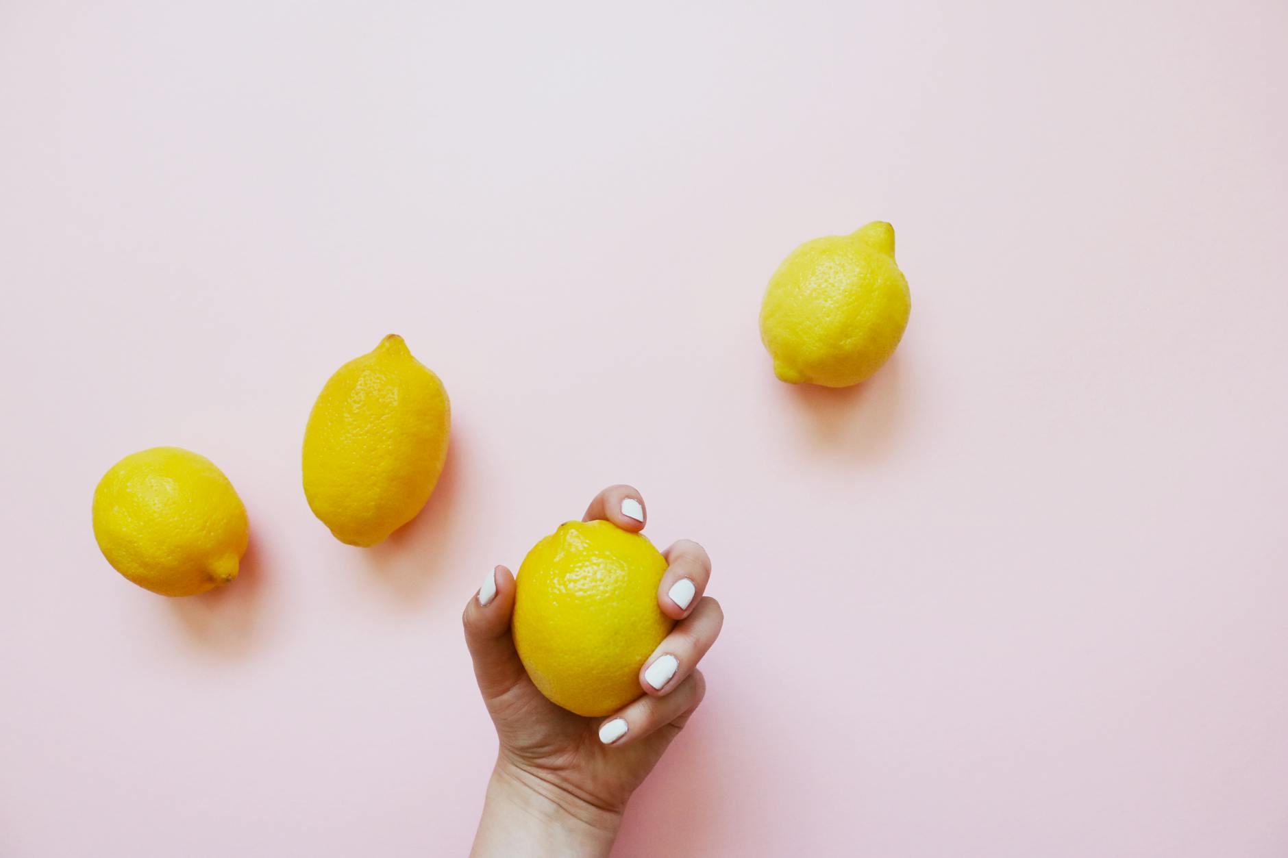 A hand holding a fresh lemon on a soft pink background, representing recovery and renewal