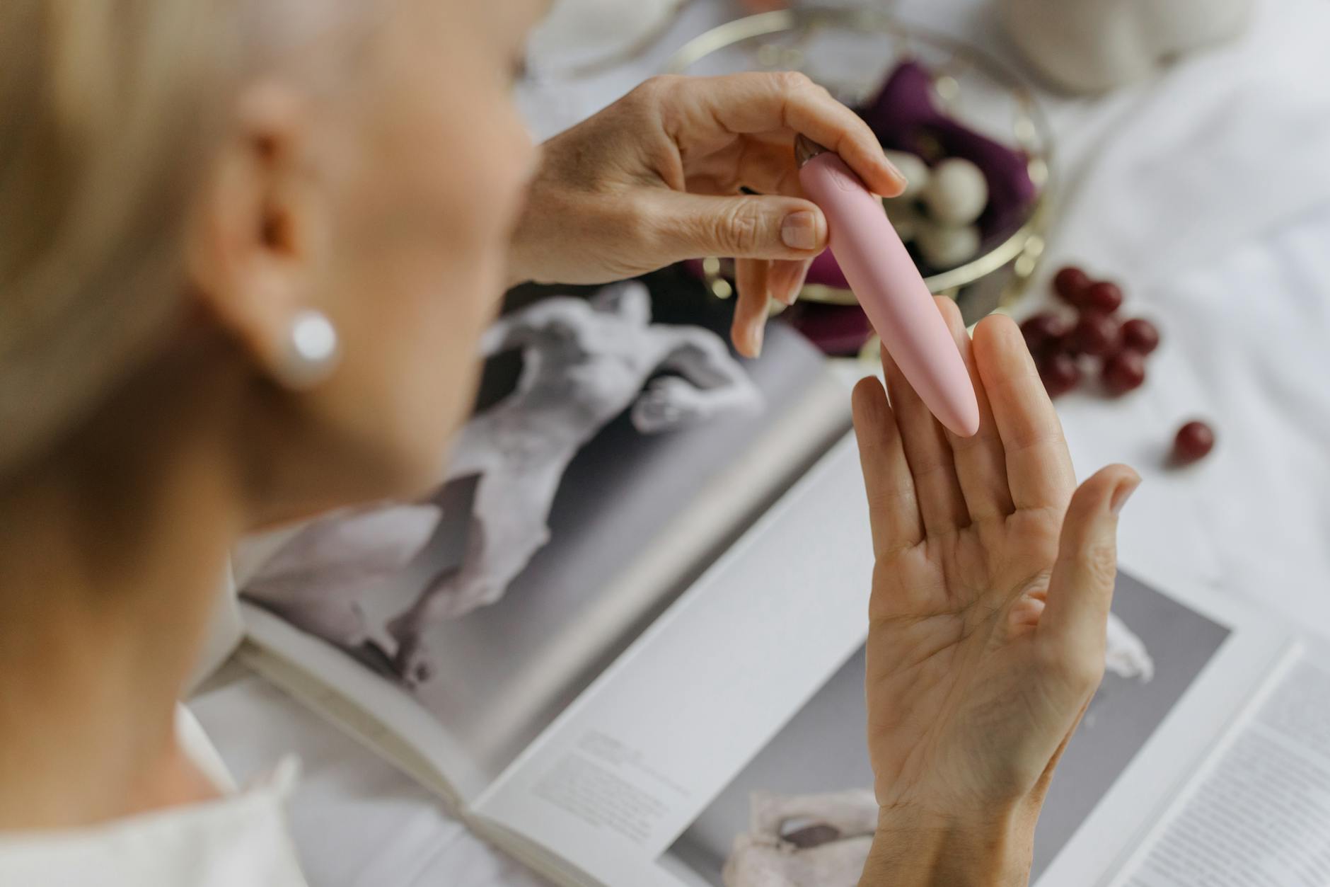 Close-up of hands holding a pink vibrator with art books in the background, symbolizing intimate couple's exploration