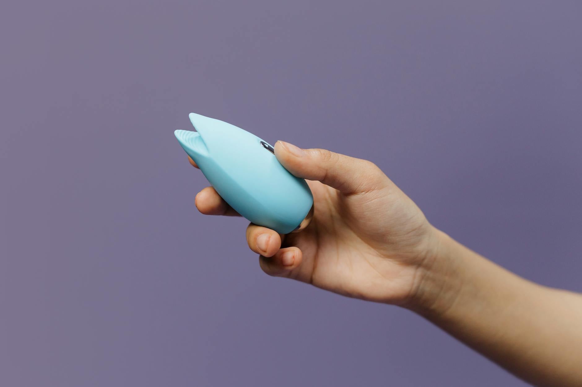 A blue silicone clitoral vibrator held in hand, representing pleasure and self-care
