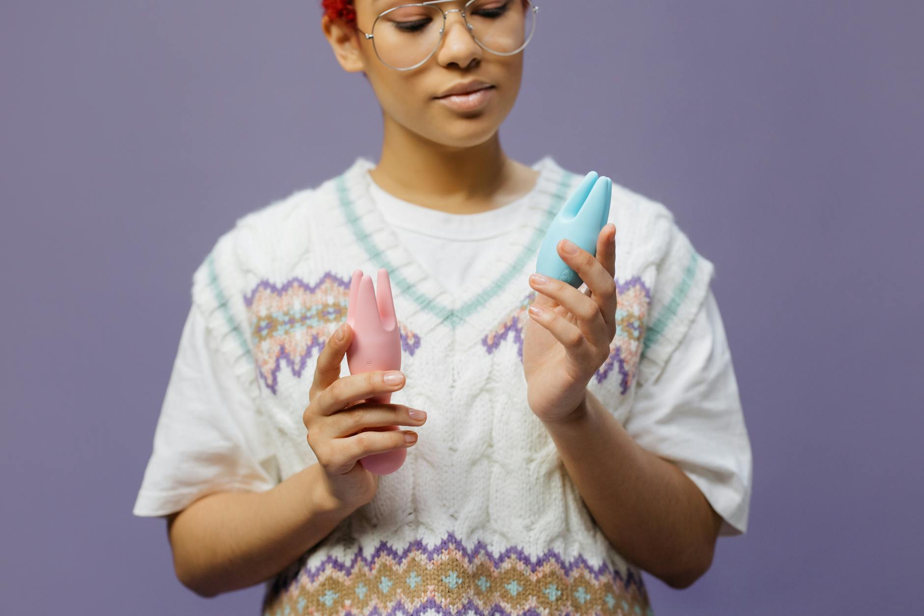 Woman contemplatively holding blue and pink silicone vibrators, representing choice and pleasure.