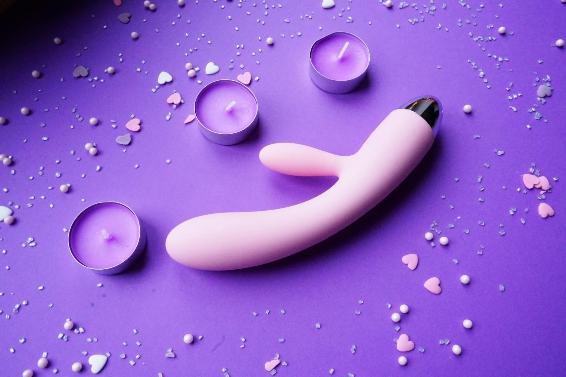 Pink vibrator on purple background with heart confetti and candles for romantic ambiance